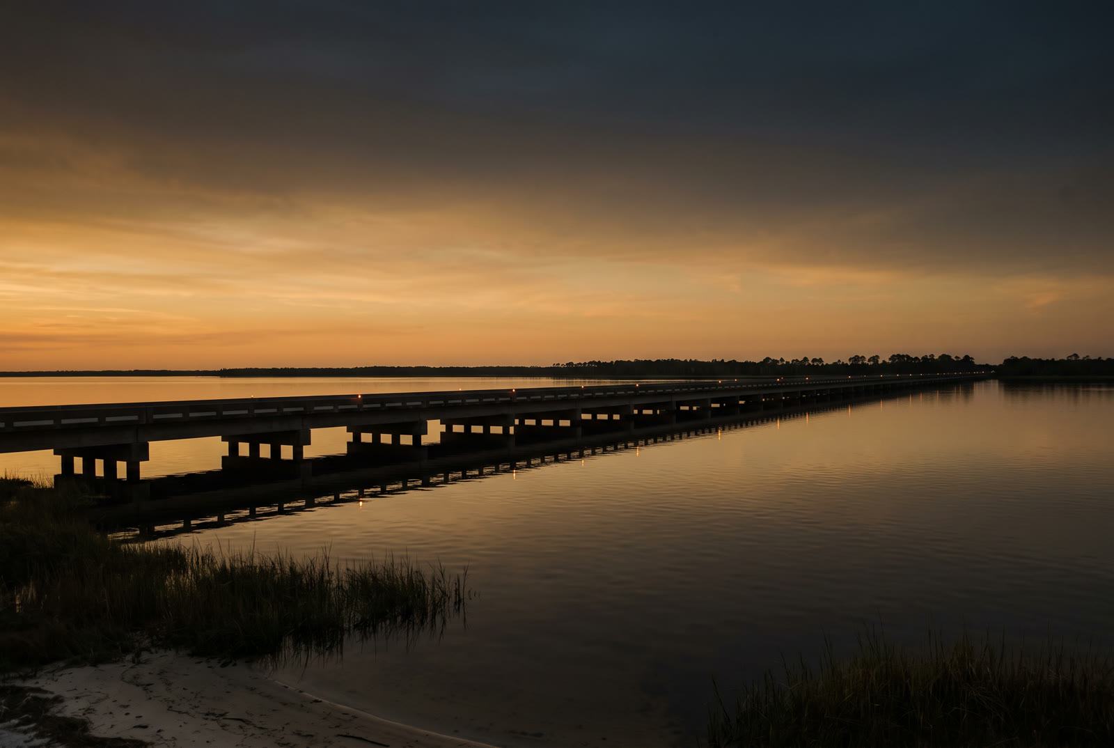 A long causeway bridge over a calm bay at dusk, illustrative
